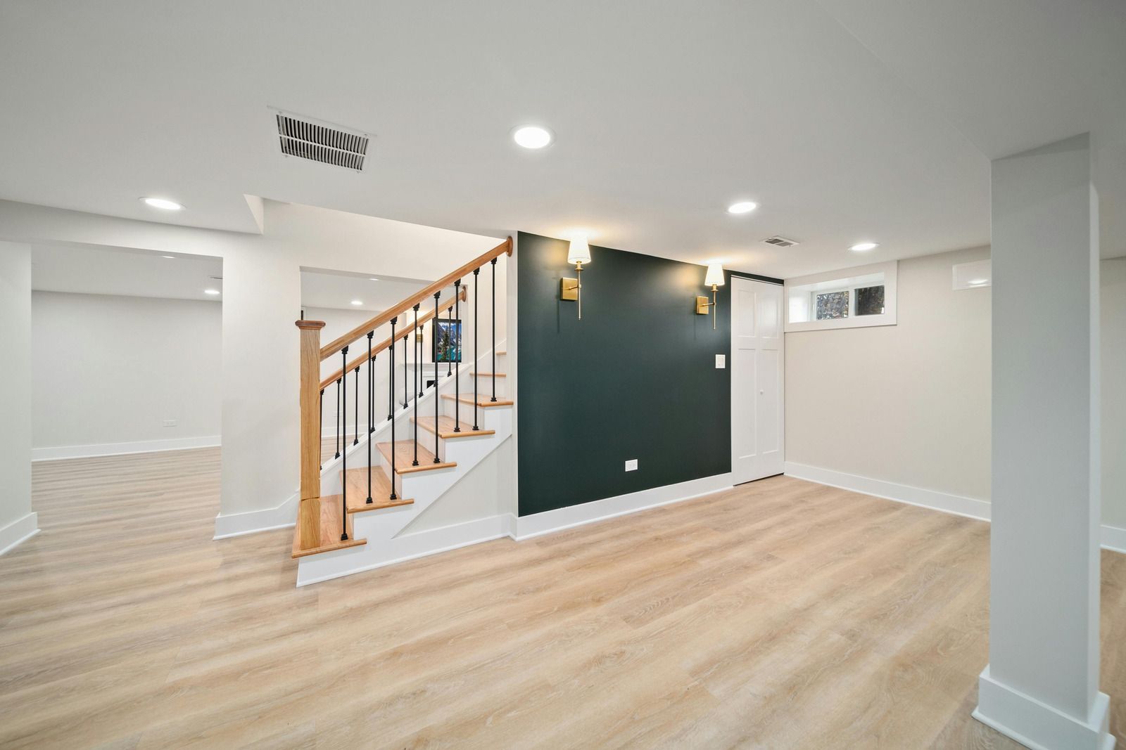 Bright empty room with wood floors, dark green accent wall, and staircase with wooden railing