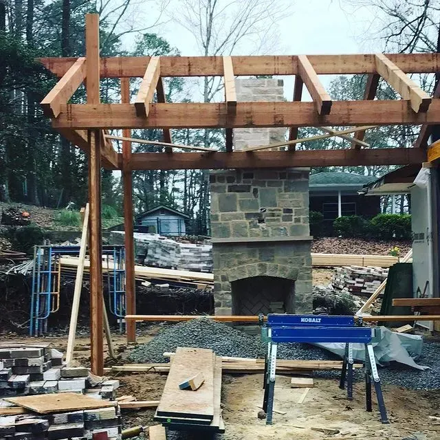 Partially built wooden pergola with stone fireplace and construction tools in a yard