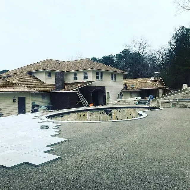 Damaged house with collapsed roof and an empty backyard pool under repair