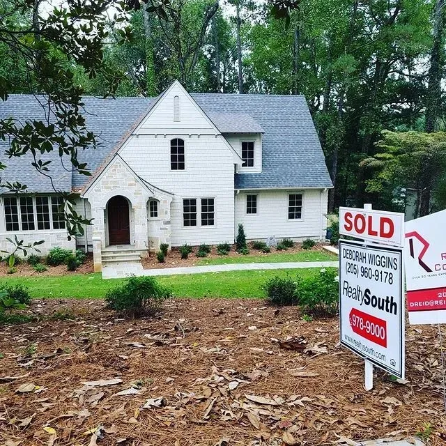 White house with a SOLD real estate sign in front, surrounded by trees and a wooded yard