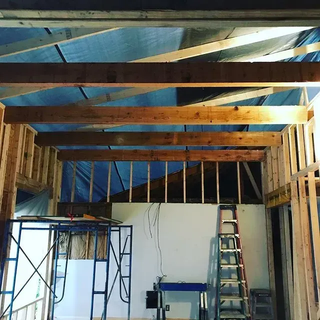 Partially framed interior with exposed ceiling beams, ladder, scaffolding, and hanging wires
