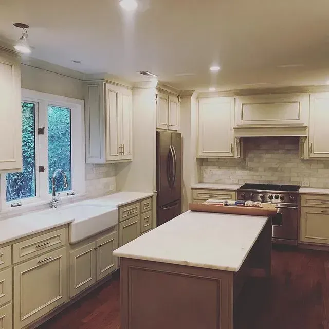 Bright cream kitchen with island, white cabinets, farmhouse sink, stainless stove, and hardwood floors