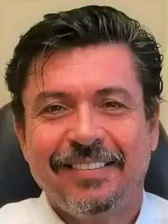 A man with a beard and mustache is smiling while sitting in a chair.