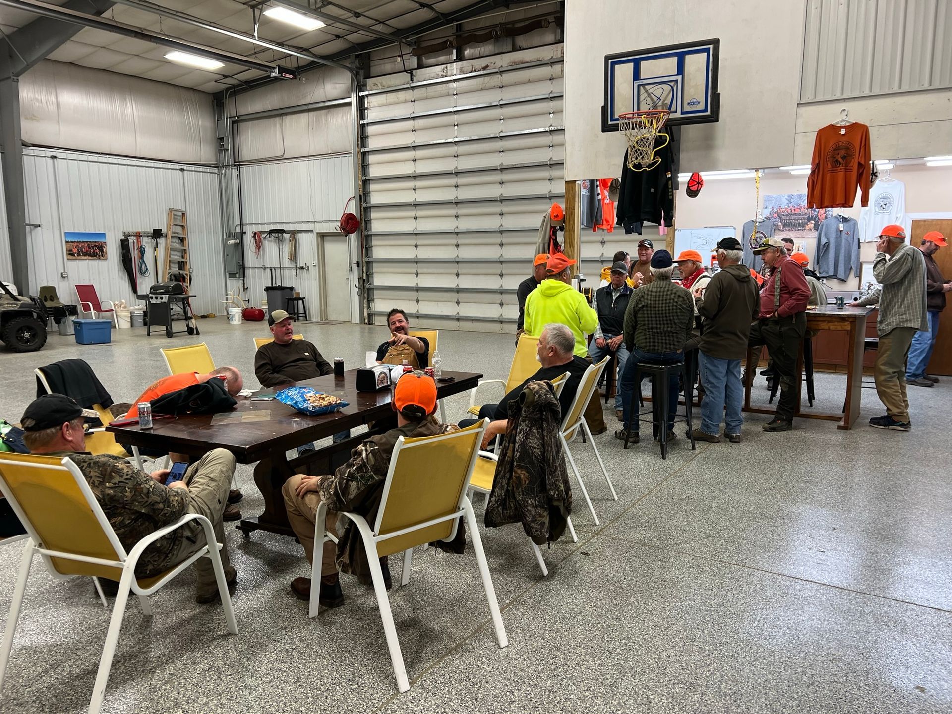 A group of men are sitting at tables in a room with a basketball hoop on the wall.