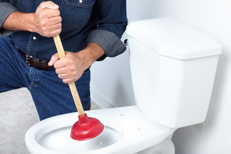 Plumber with plunger to clean a toilet