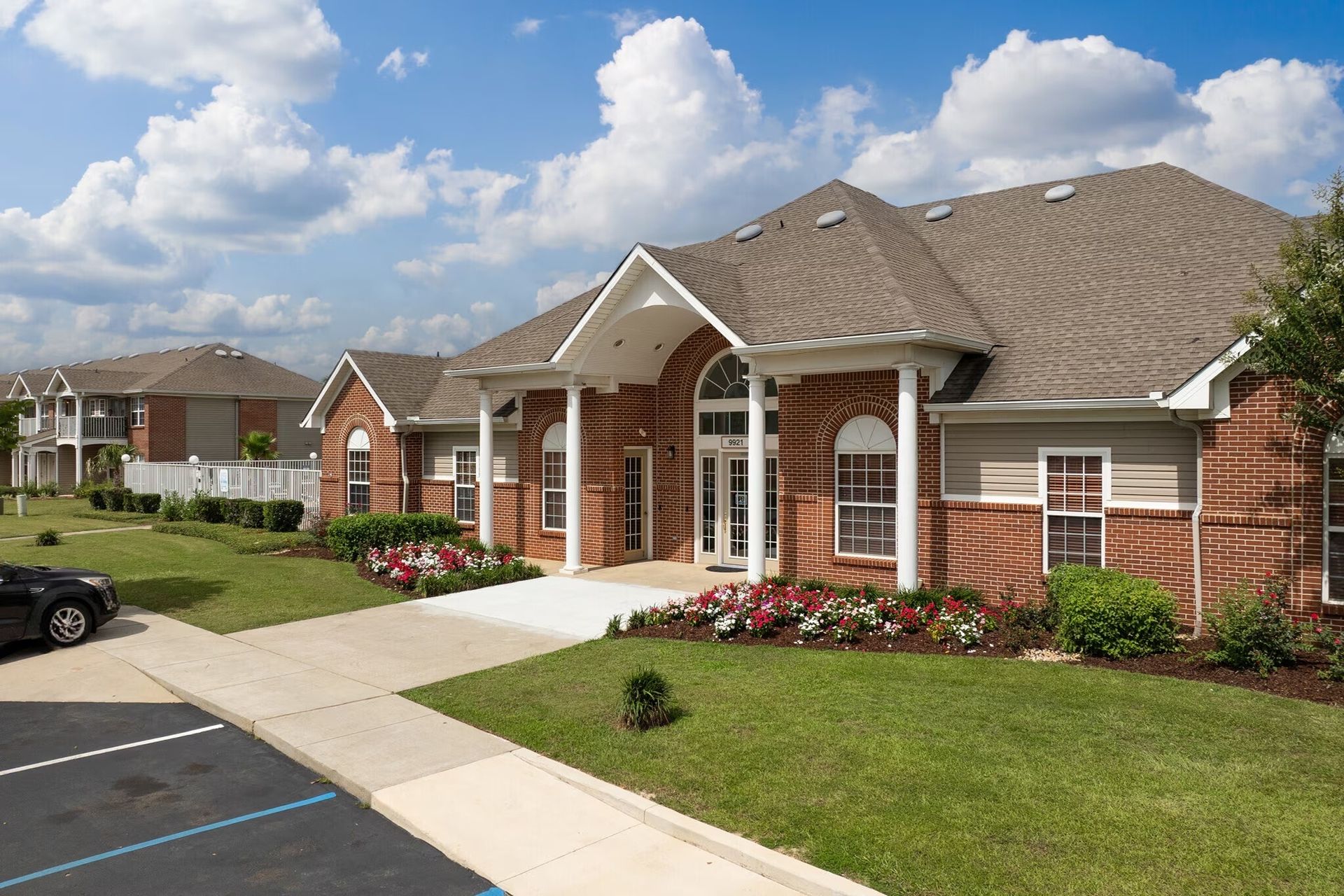 Brick building with white trim, arched entryway, and green lawn under a partly cloudy sky.