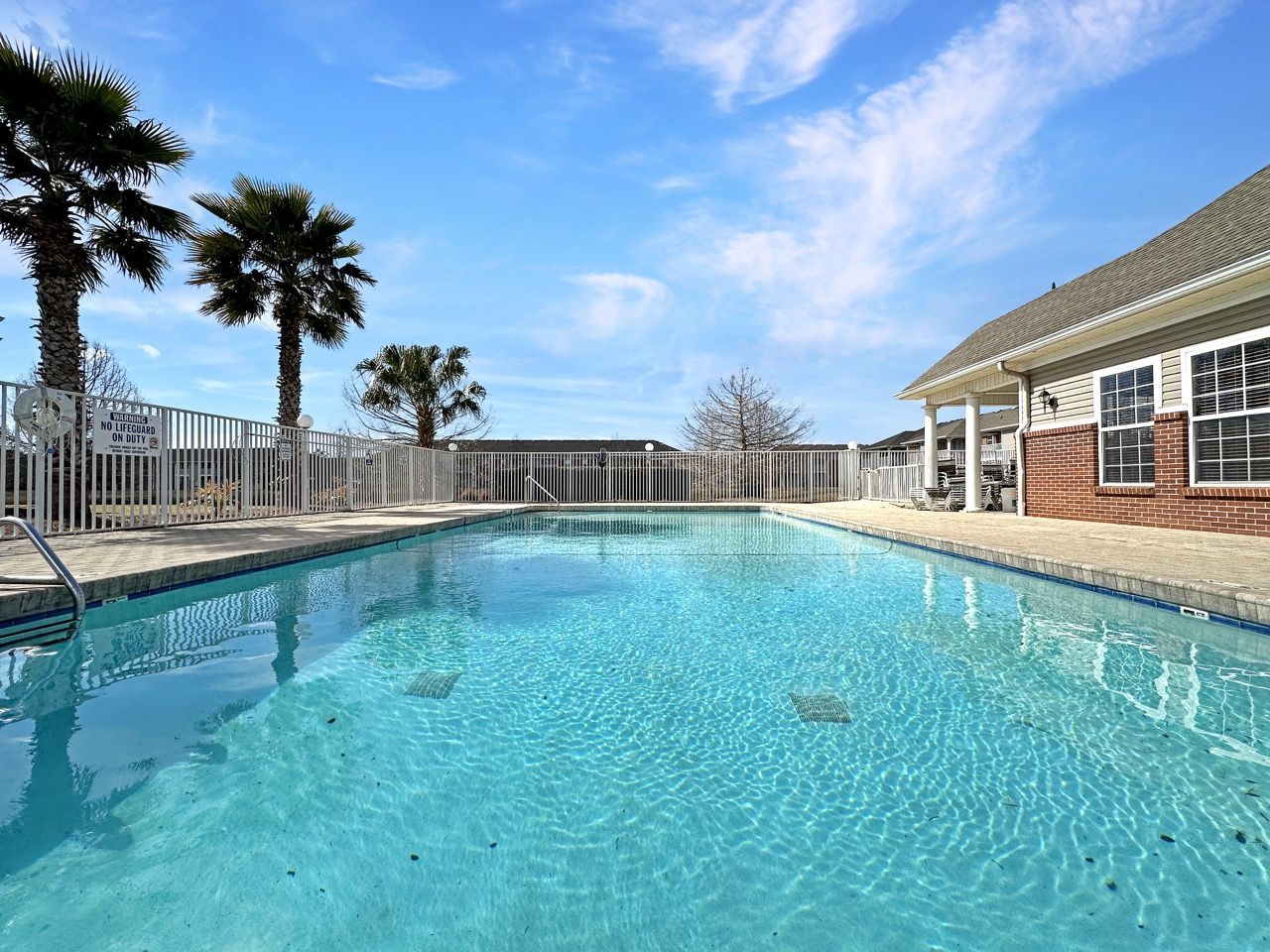 Swimming pool with palm trees under a blue sky, next to a building.