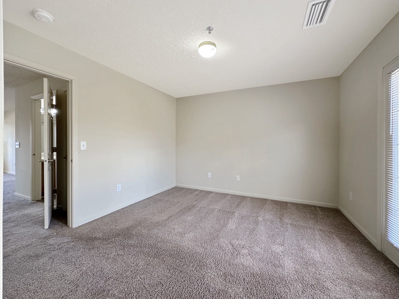 Empty room with beige walls, brown carpet, and a partially open door to the left.