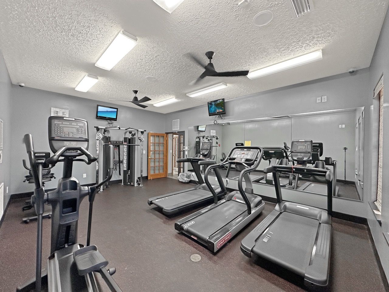 Gym interior with treadmills, elliptical, exercise equipment, mirrors, and TVs.