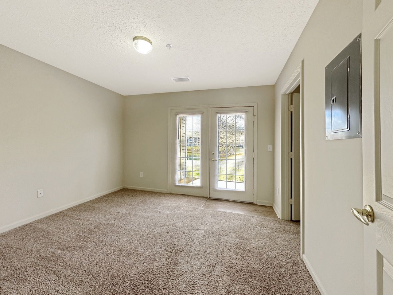Room with beige walls, brown carpet, double doors to outside, and an electrical panel.