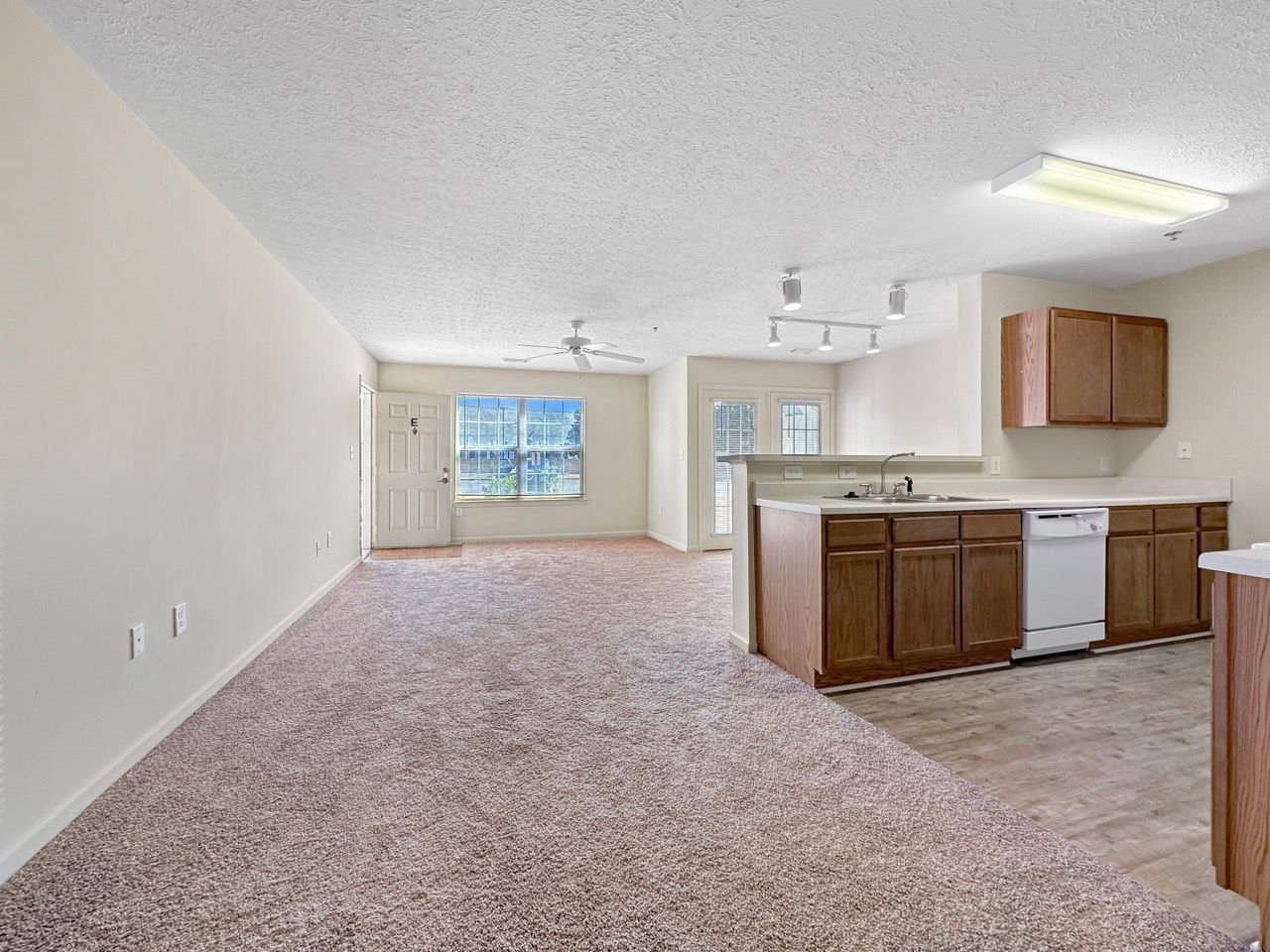 Open-plan living space with kitchen and living room; brown cabinets, white appliances, and brown carpet.