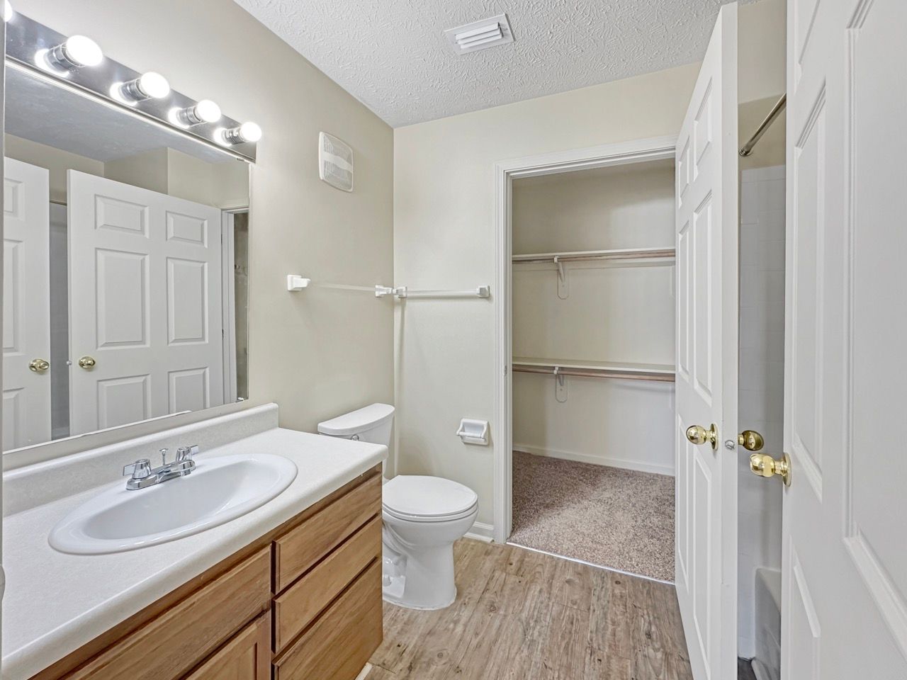 Bathroom with wood cabinets, white sink, toilet, towel rack, closet, and open door.