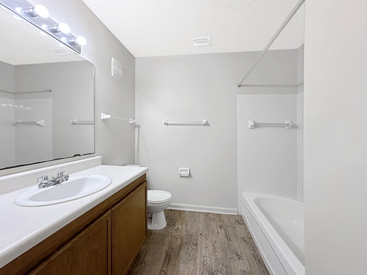 Bathroom with a white tub, sink, and toilet; gray walls and wooden floor.