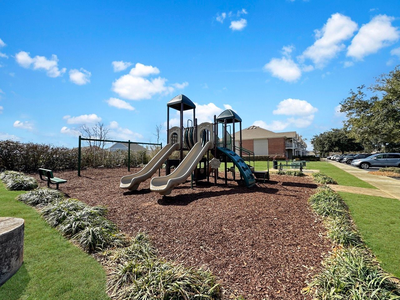 Playground with slides, swings, and mulch ground cover on a sunny day.