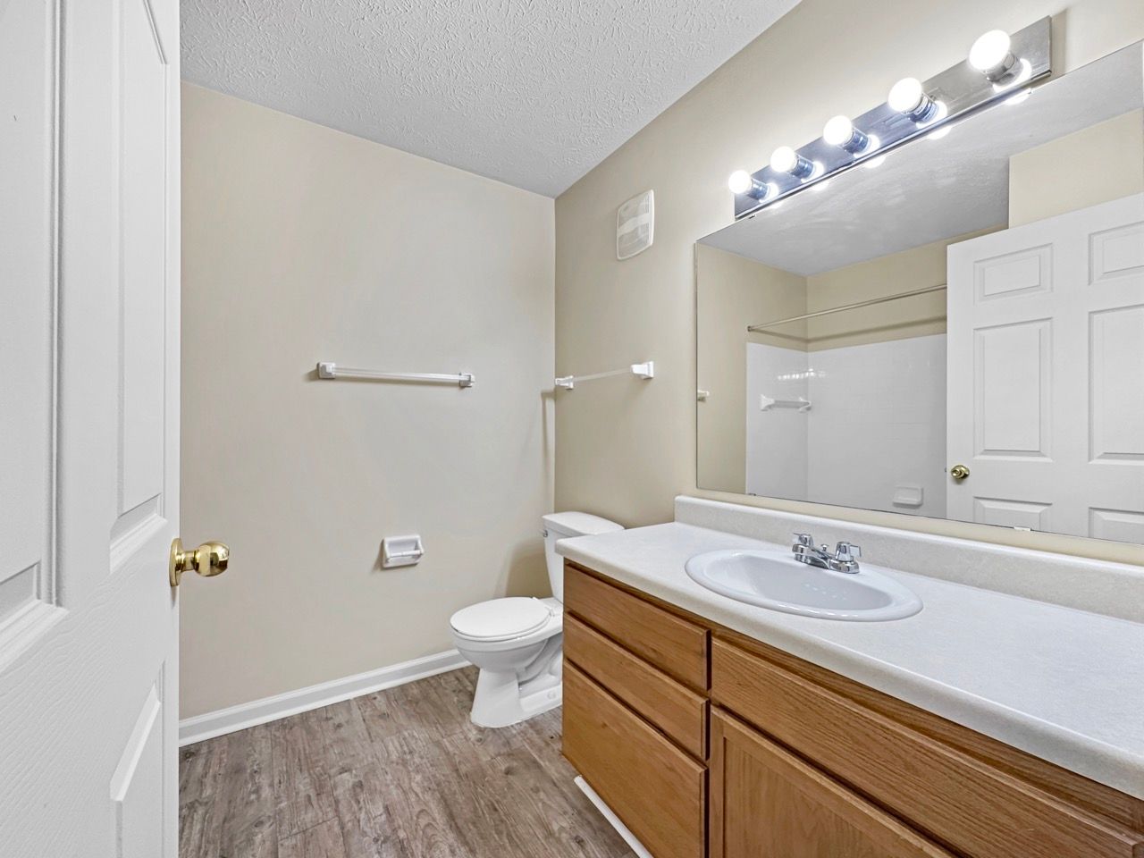 Bathroom with vanity, toilet, and shower. Beige walls, wood cabinets, and gray flooring.