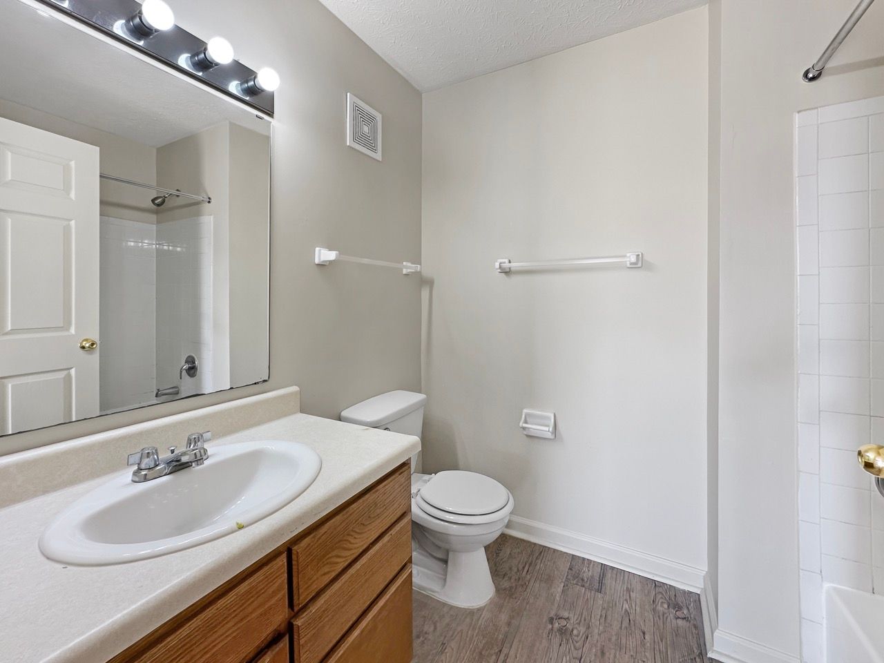 Bathroom with a vanity, toilet, and shower. Gray walls, brown cabinets, and wood-look flooring.