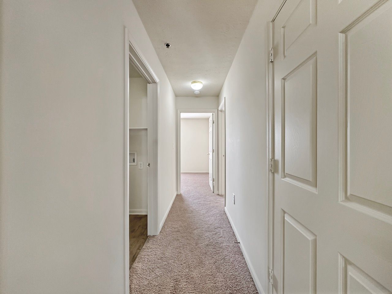 Narrow hallway with carpet, white walls, and doors leading to other rooms.
