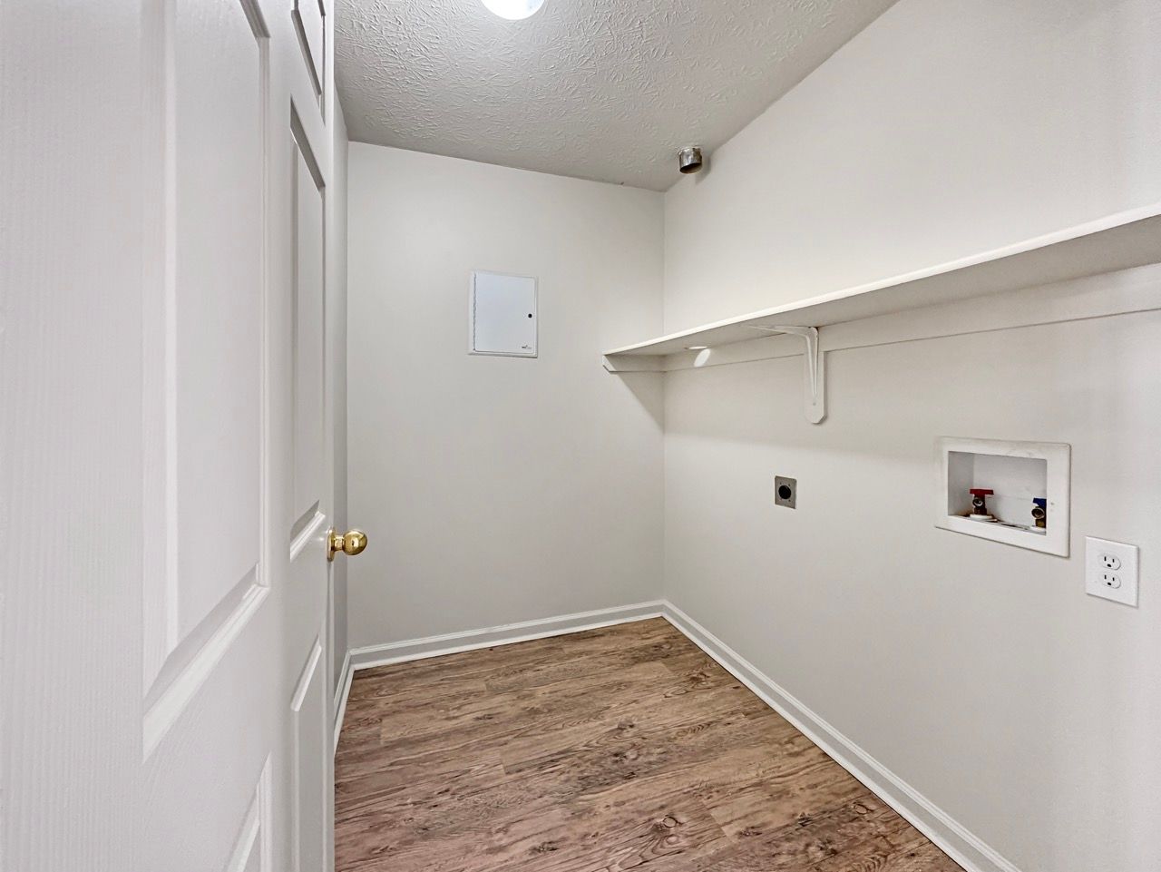 Laundry room with white walls, wooden floor, shelf, and washer/dryer hookups.