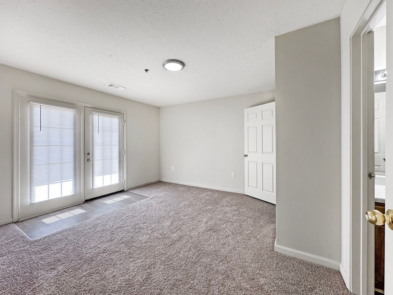 Empty room with carpet, French doors, and a closed white door.