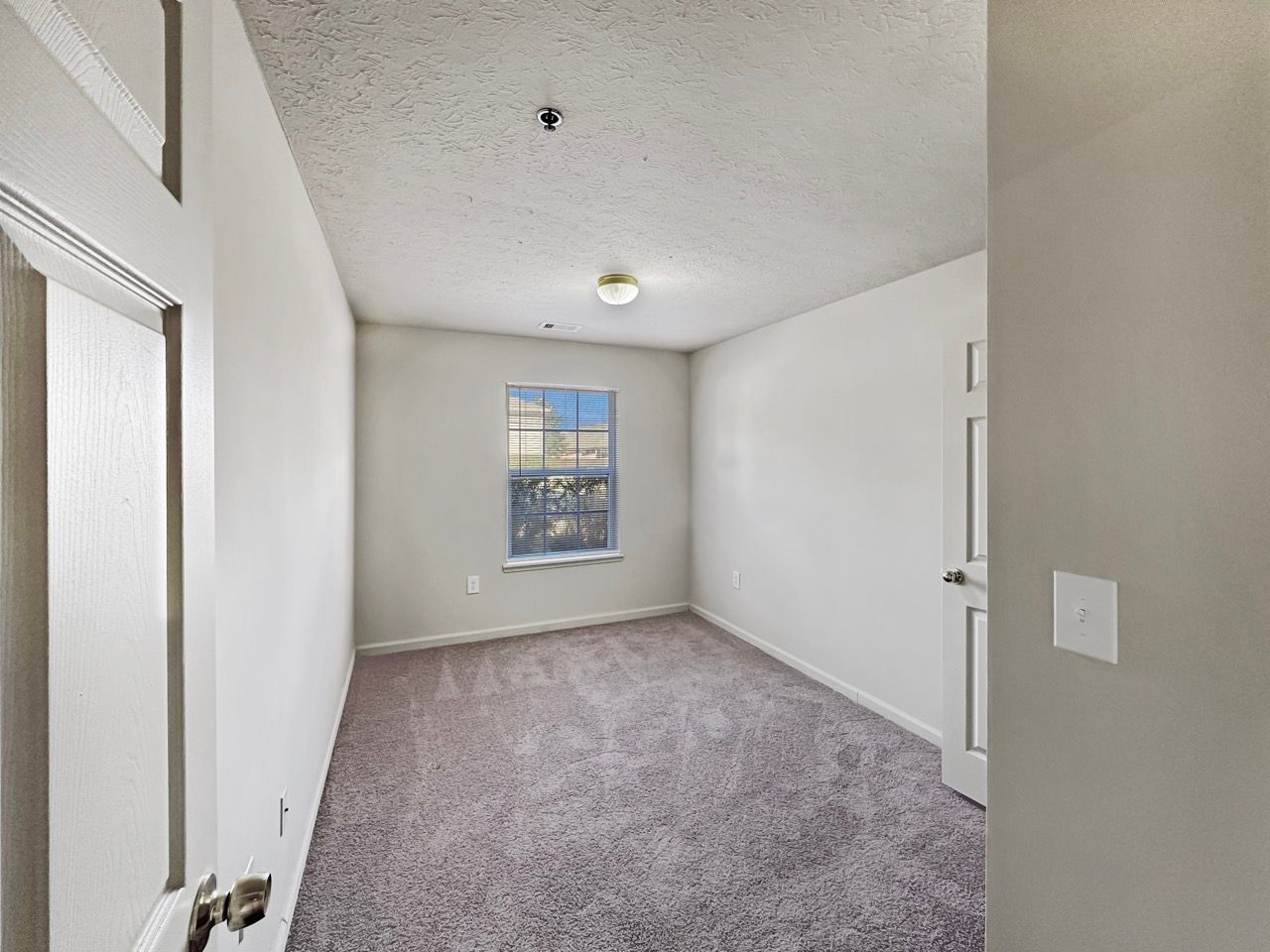 Empty bedroom with carpet, window, and two doors, all light-colored.