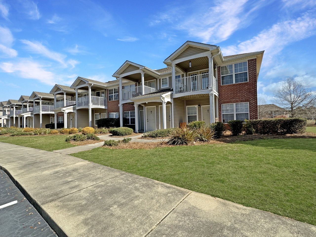 Multi-story apartment building with balconies, brick and siding exterior, green lawn, blue sky.