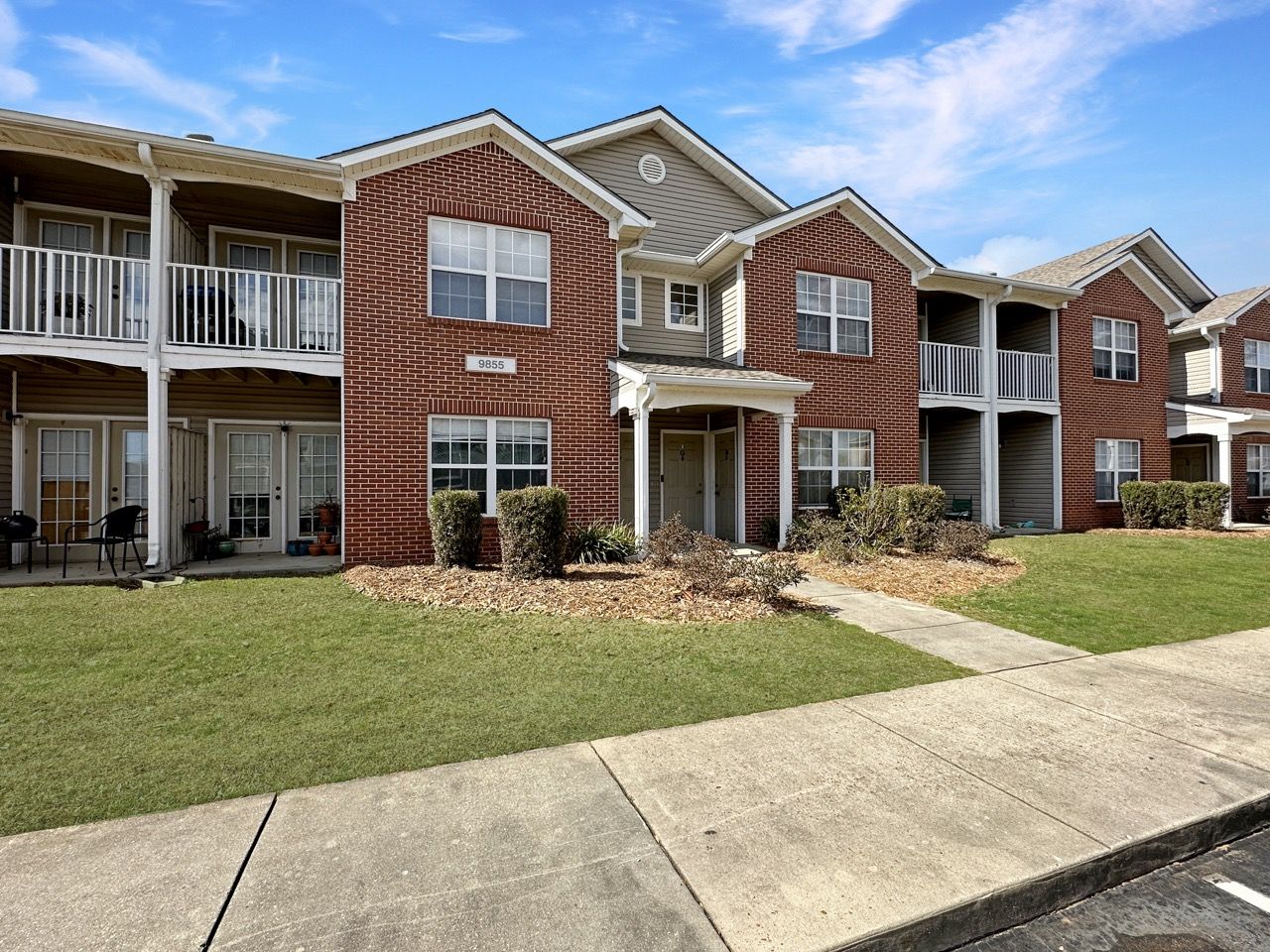 Apartment complex with brick facade, two stories, balconies, and green grass.