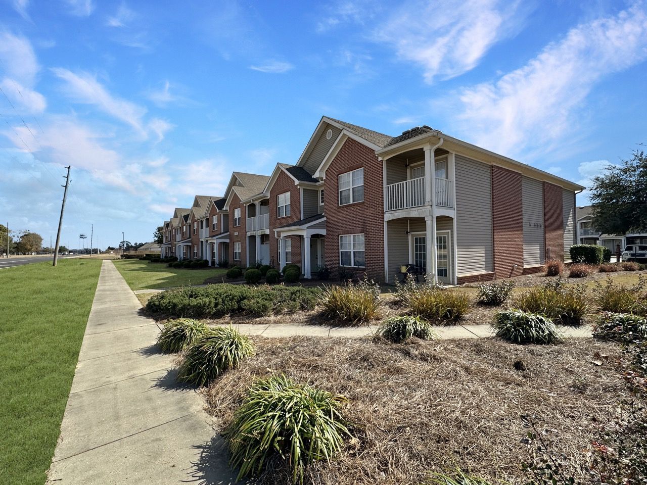 Apartment buildings with brick facade, two stories, sidewalk, grass, and a blue sky.