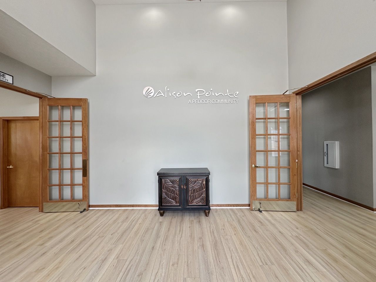 Wooden-floored room with two glass-paned doors and a cabinet against a light gray wall.