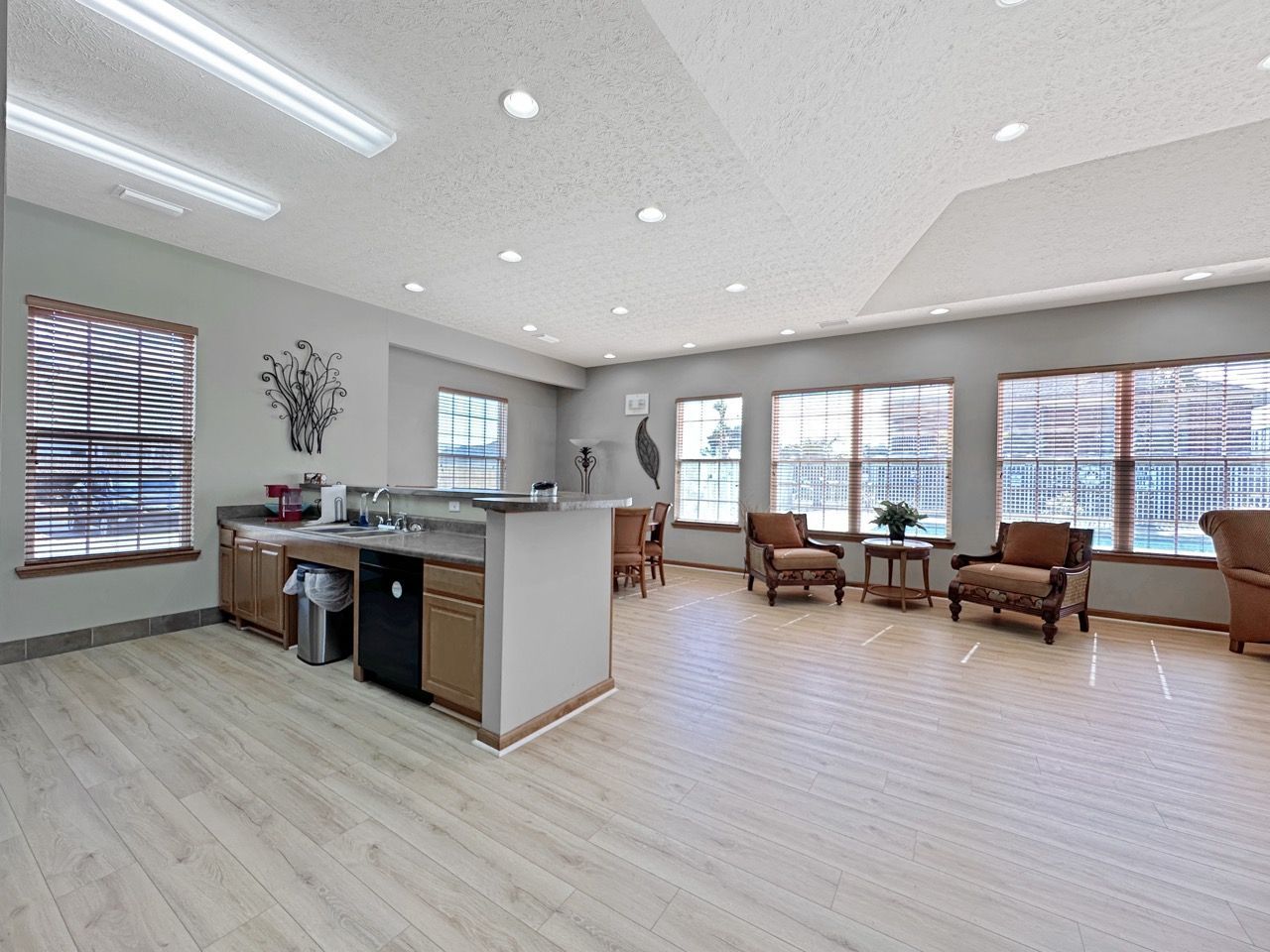 Open-plan lounge with kitchenette, multiple windows, seating, and light wood flooring.