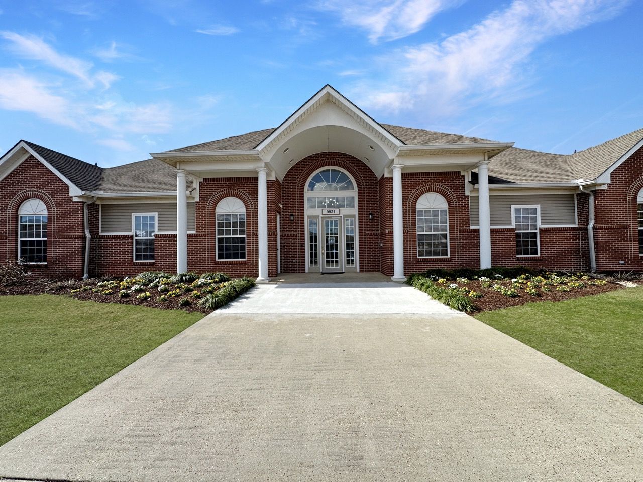 Brick building with arched entryway, white pillars, and a concrete walkway.