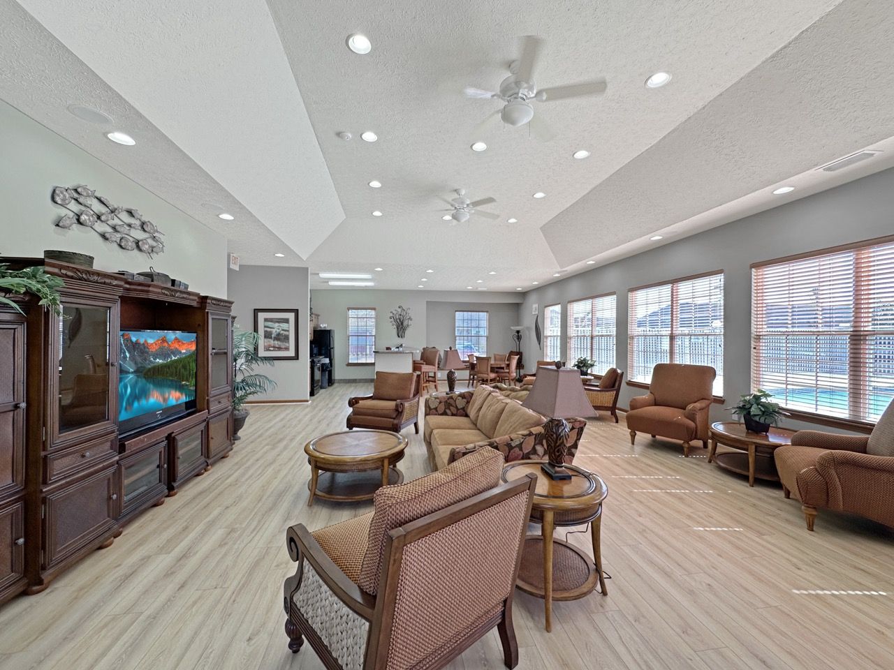 Spacious lounge with brown furniture, TV, and large windows overlooking a pool.