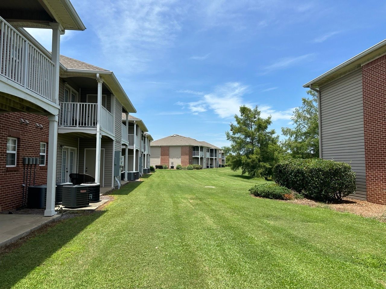 Apartment complex exterior with a grassy lawn, blue sky, and two-story buildings with balconies.