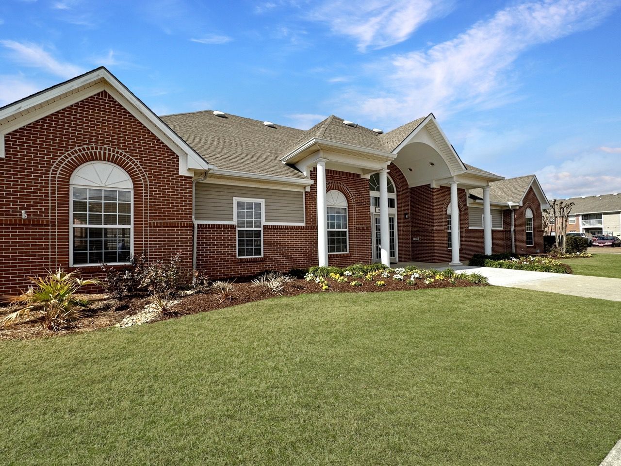 Red brick building with arched windows, white columns, and a grassy lawn under a blue sky.