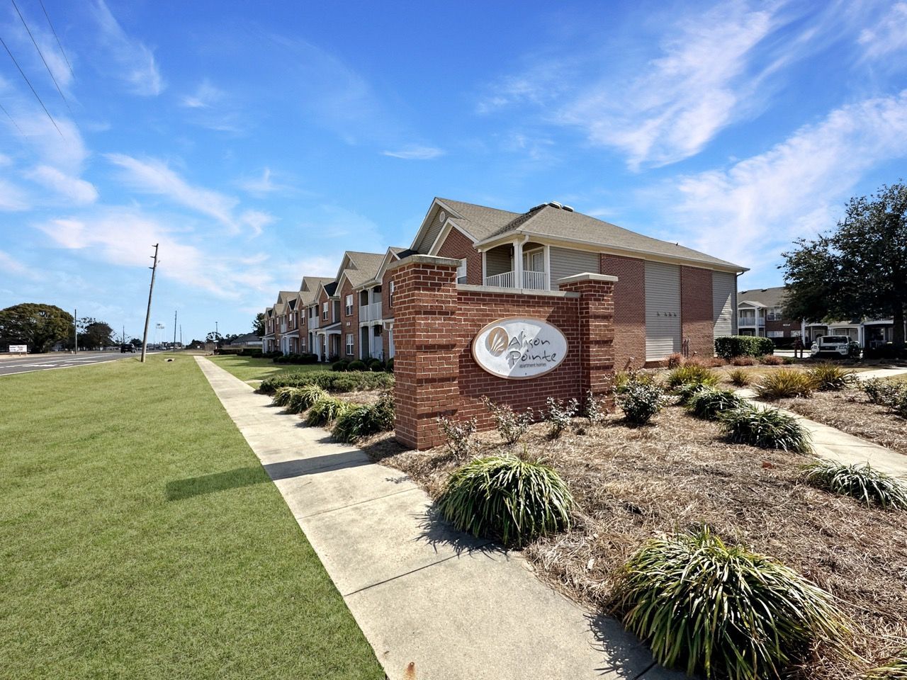 Sign for Oak Lake Village apartments beside a long row of brick buildings on a sunny day.