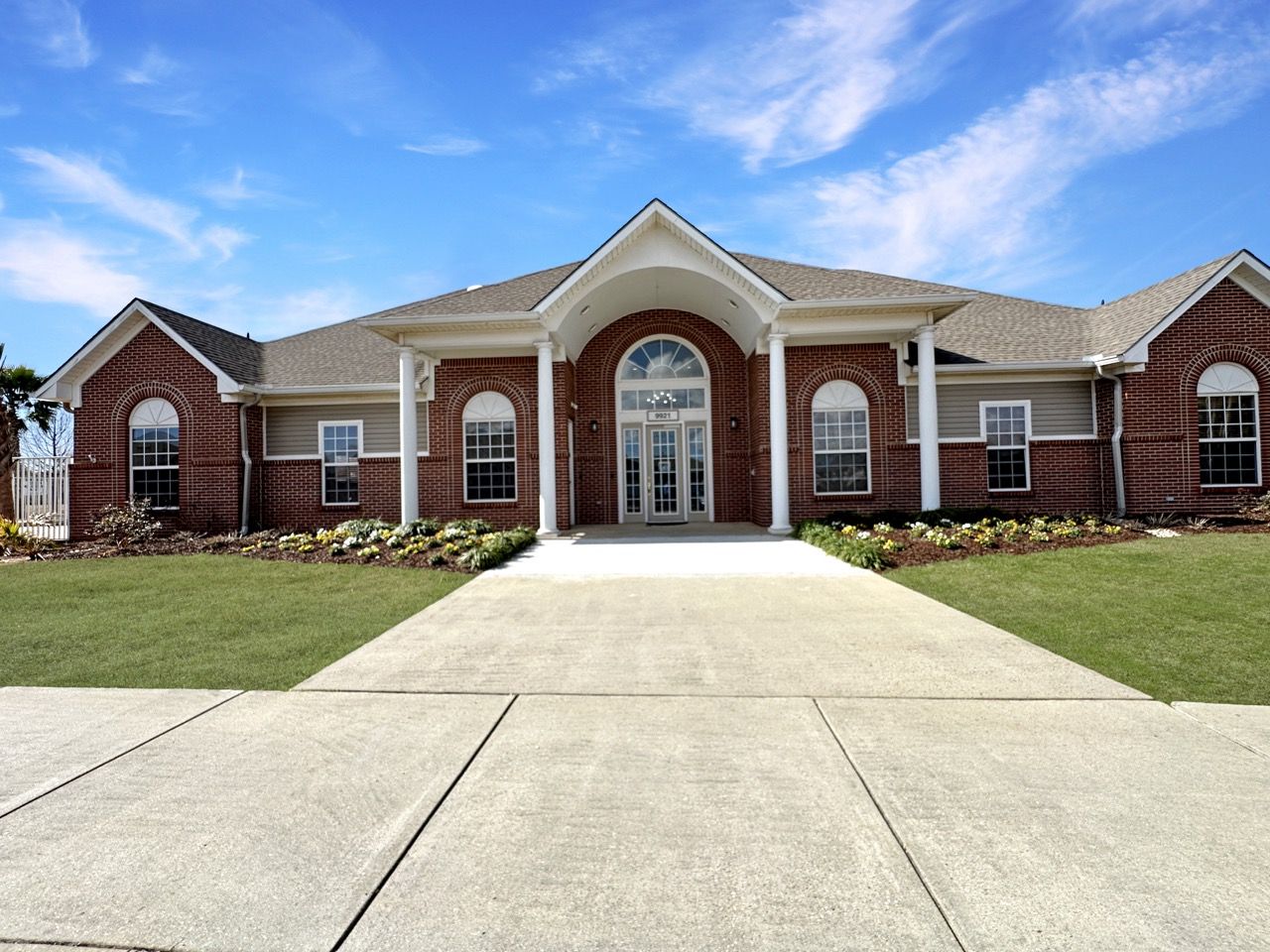 Brick building with arched entryway, white columns, and green lawn under blue sky.