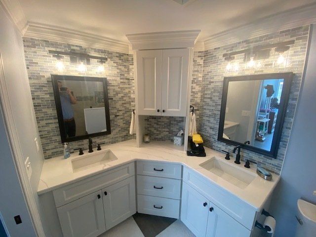 A modern bathroom with white cabinets, two sinks, mirrors, and a mosaic tile backsplash.