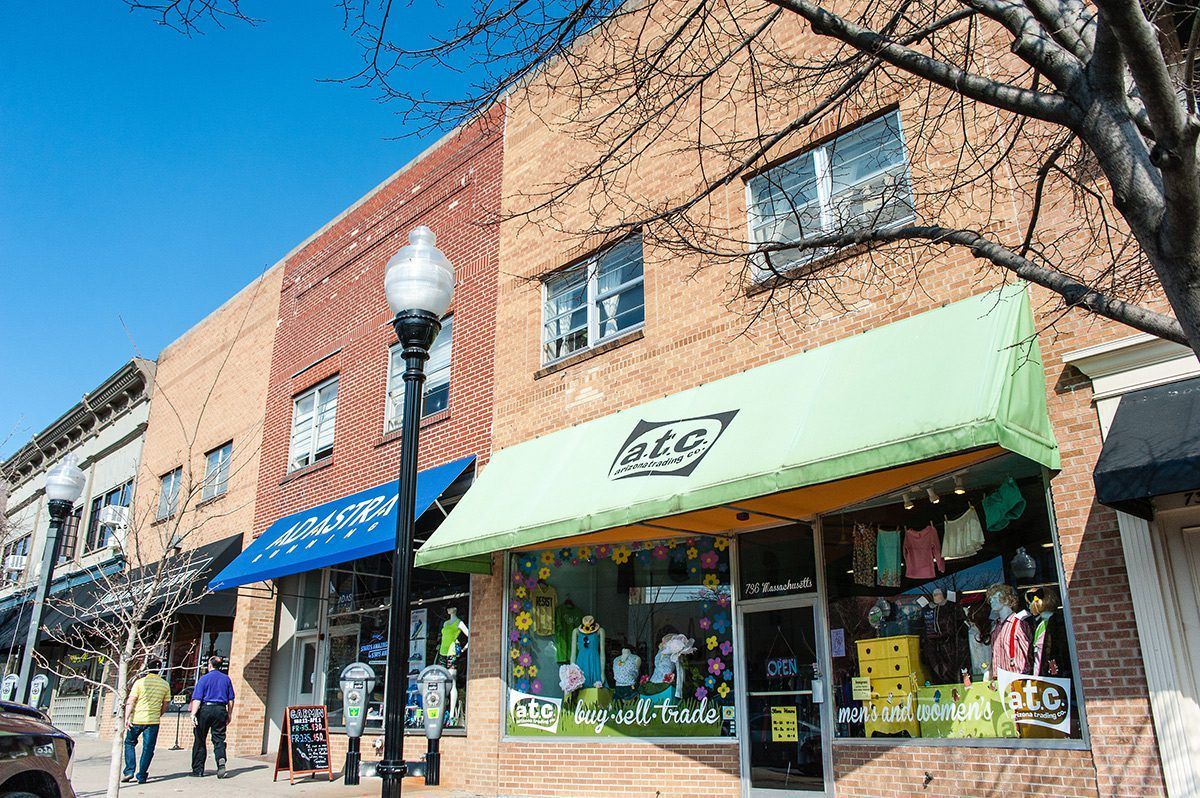 Brick storefronts with awnings; pedestrians on sidewalk; sunny day.