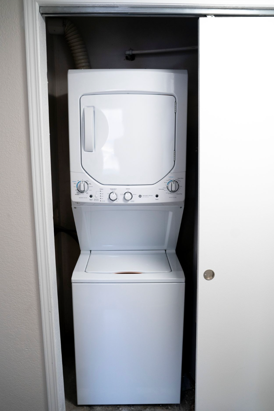 Stacked white washer and dryer unit inside a closet with a closed sliding door.