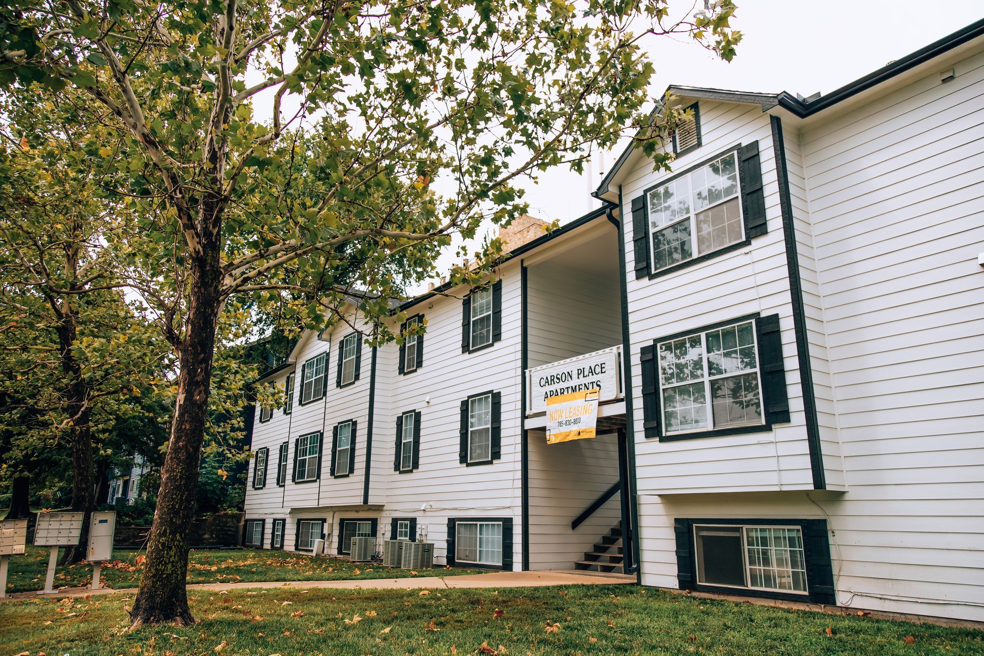 White multi-story building with black shutters and a small tree-lined yard.