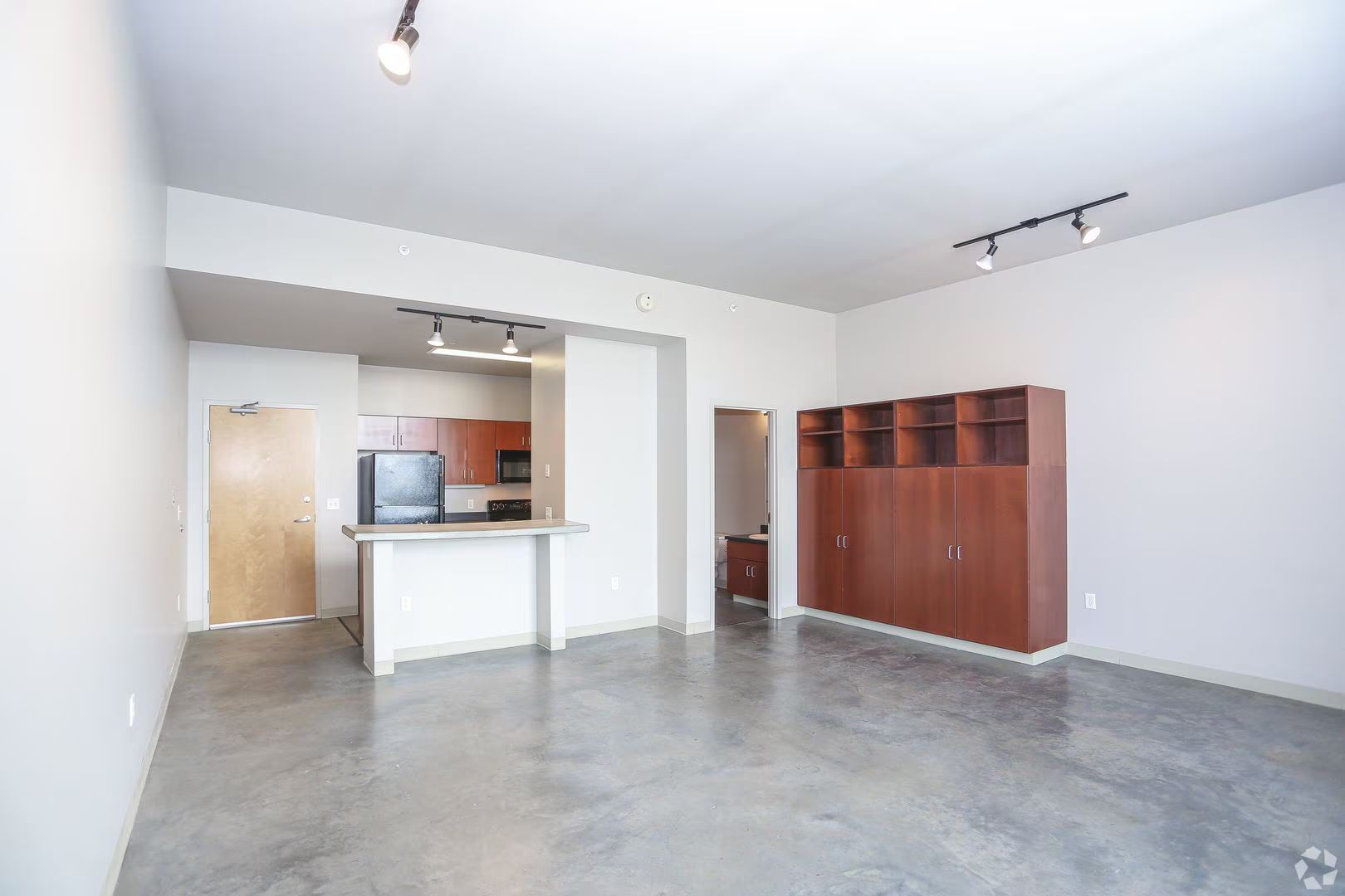 Empty apartment interior with concrete floors, kitchen, and built-in storage.
