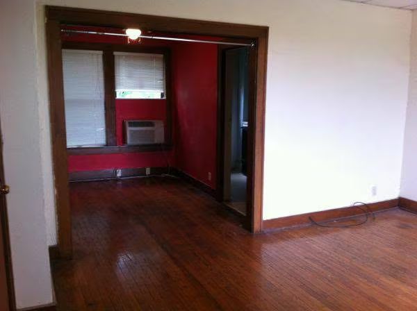 Living room with dark wood flooring, open to a white kitchen.