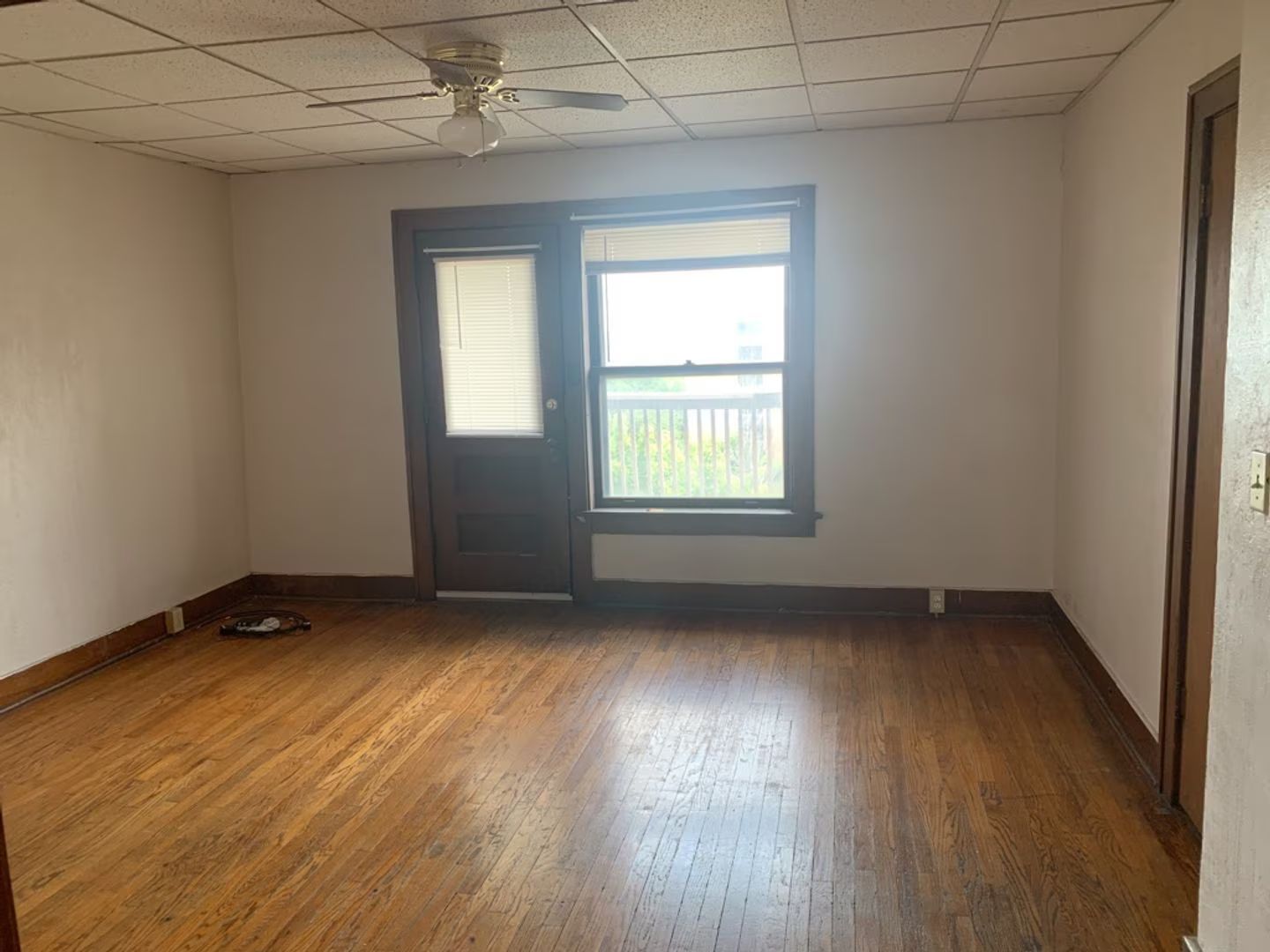 Empty living room with dark wood flooring, sliding glass door, and pale walls.
