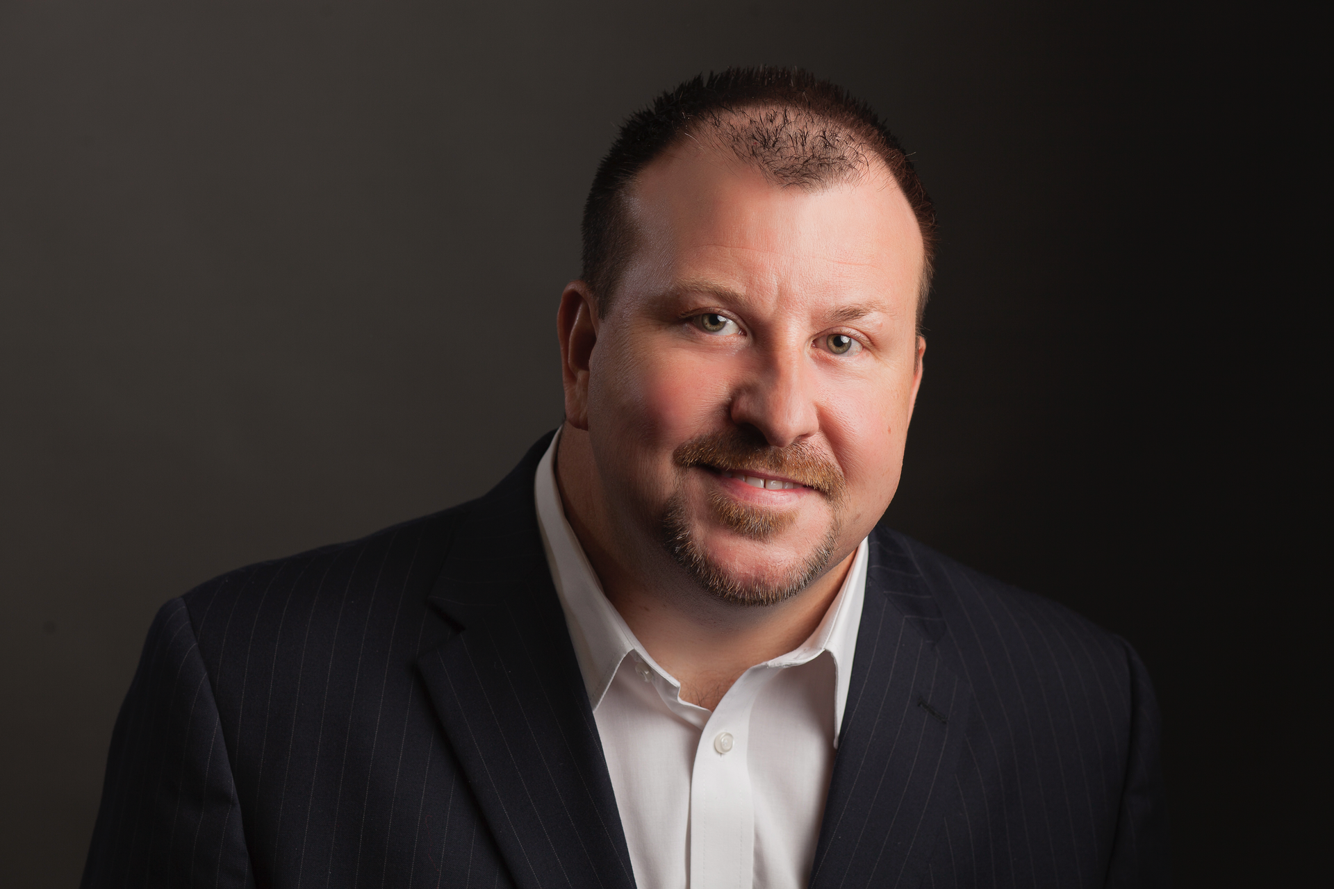 A man in a suit and white shirt is smiling for the camera.