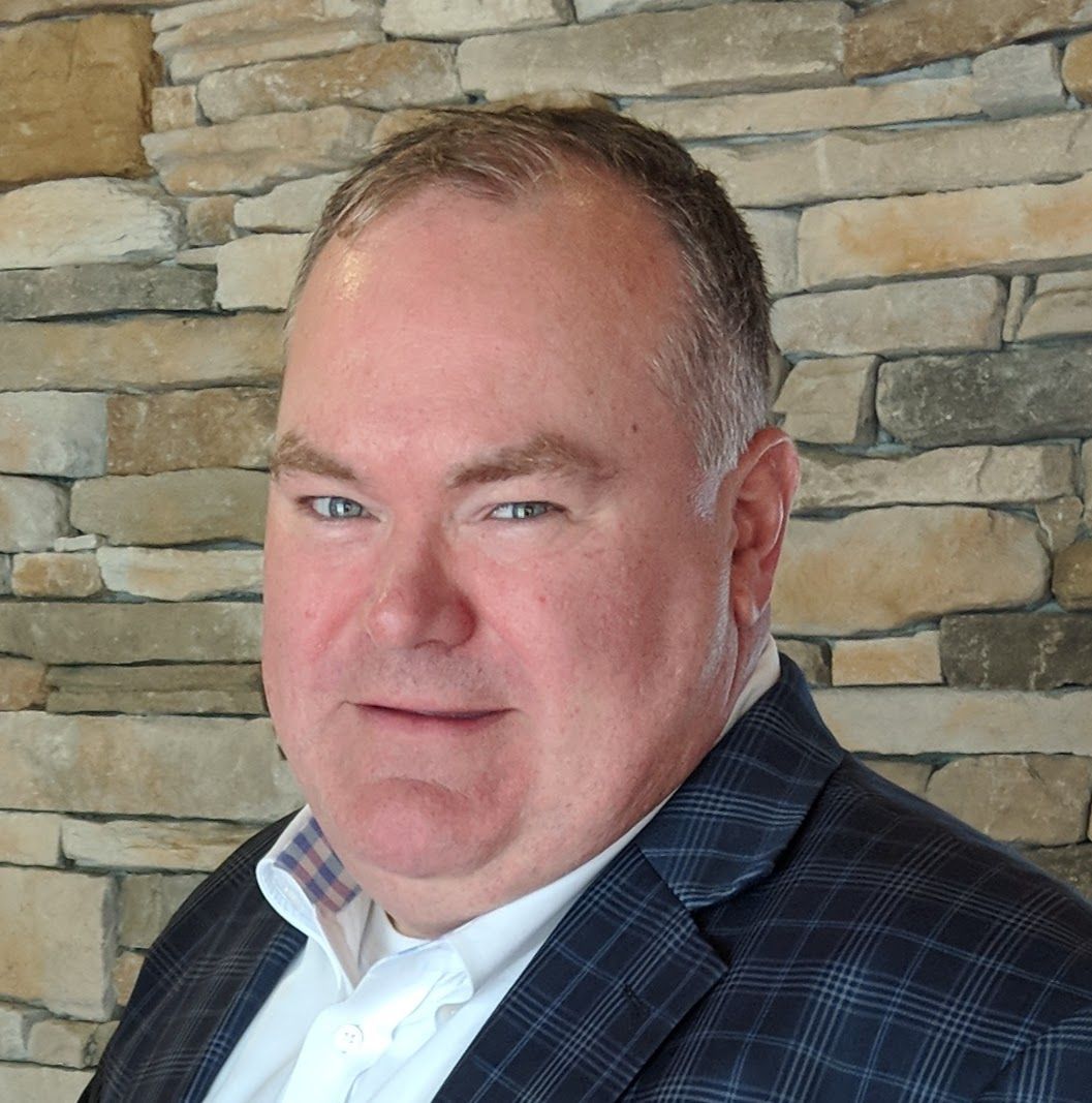 A man in a suit is standing in front of a stone wall.