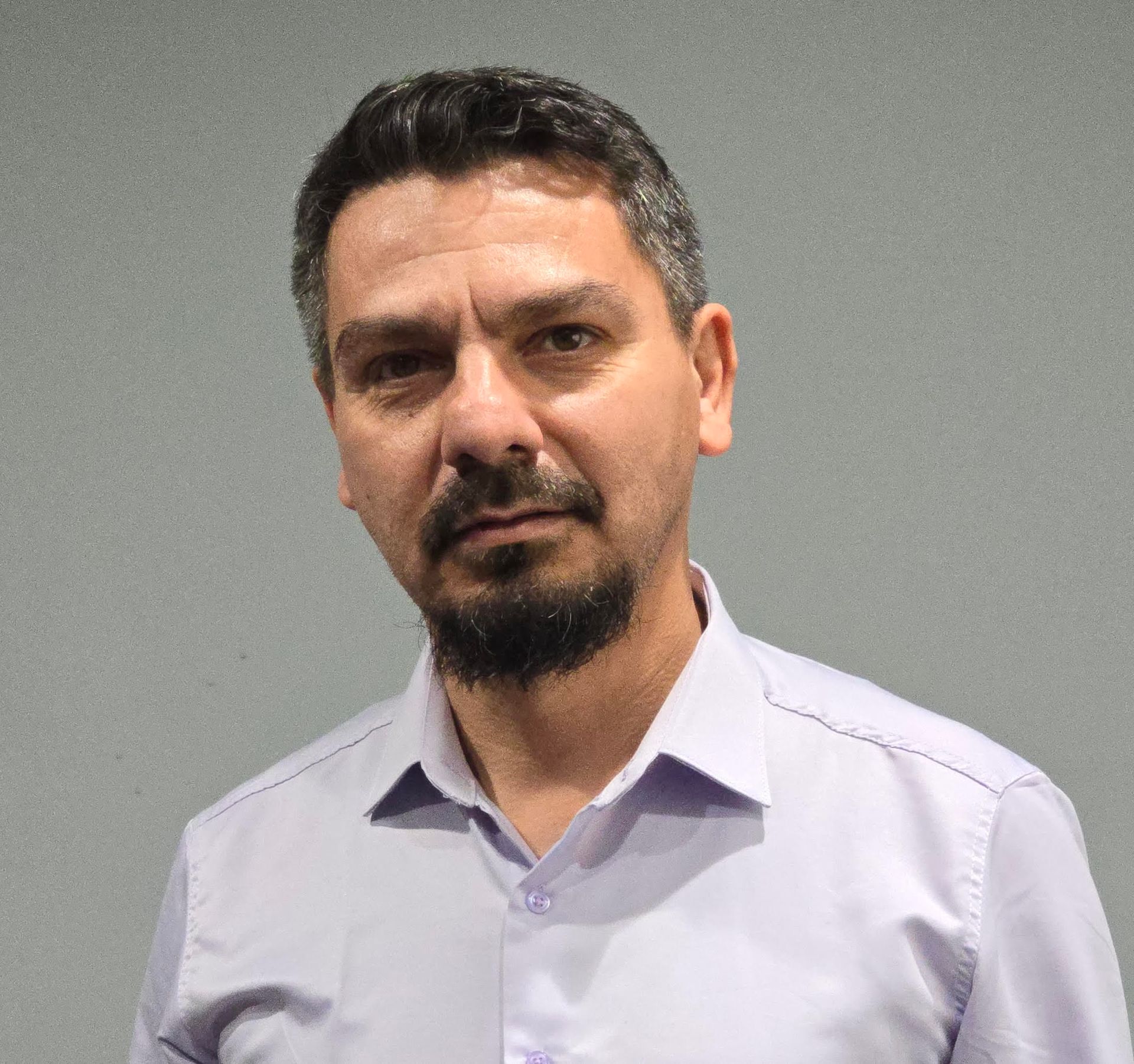 A man with a beard is wearing a purple shirt and looking at the camera.