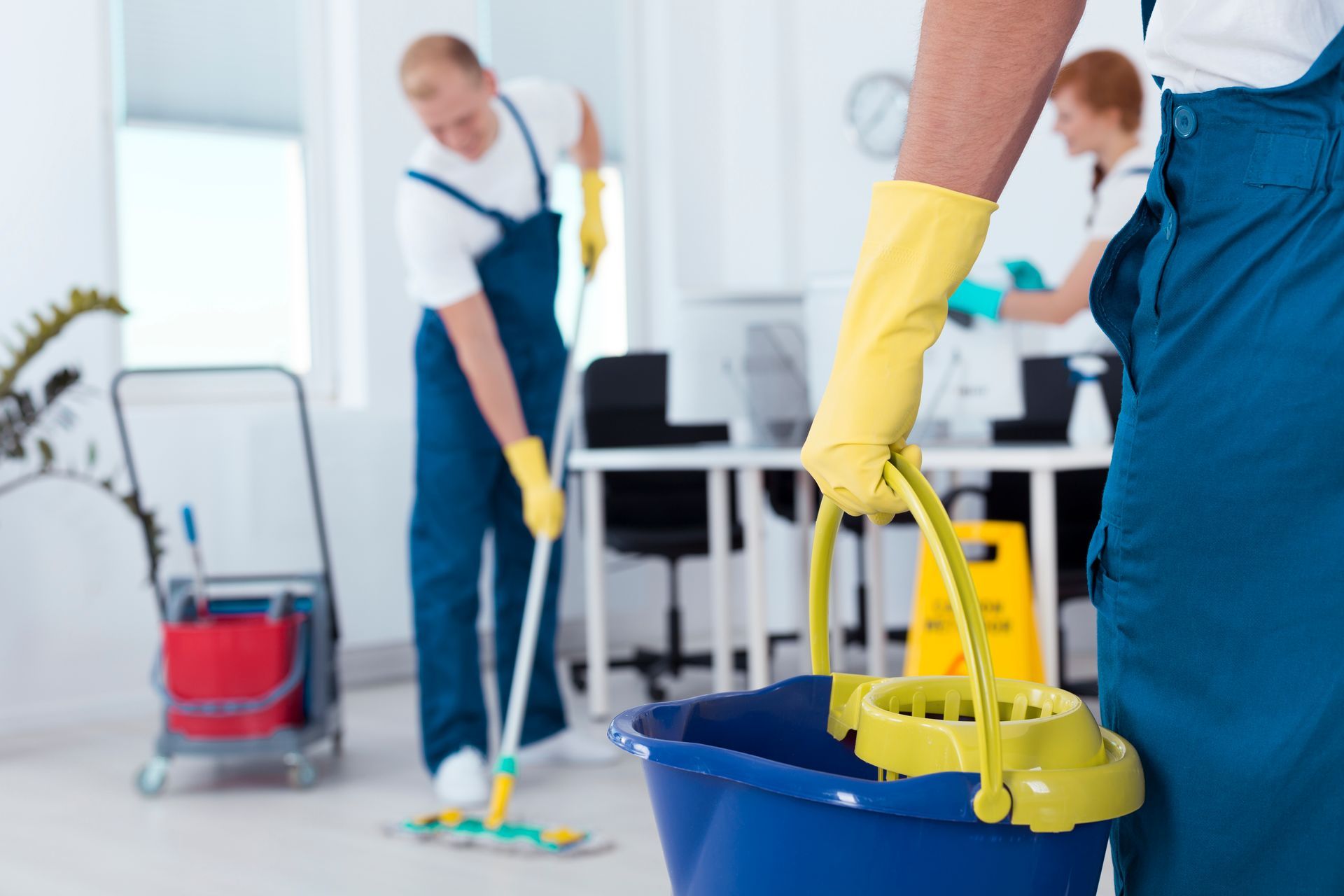 A man is holding a blue bucket and mop in an office.