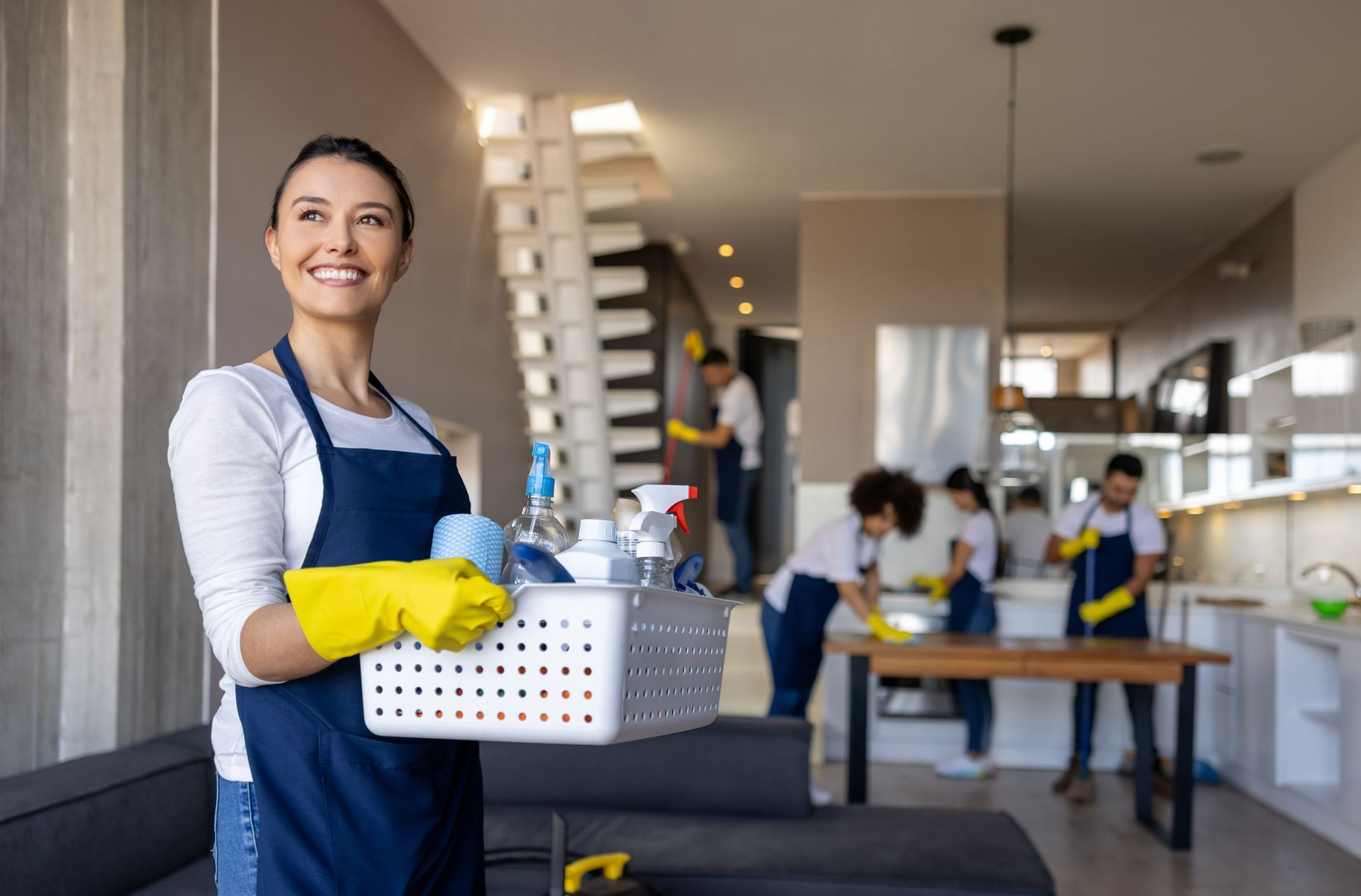 A woman is holding a basket of cleaning supplies in a living room.