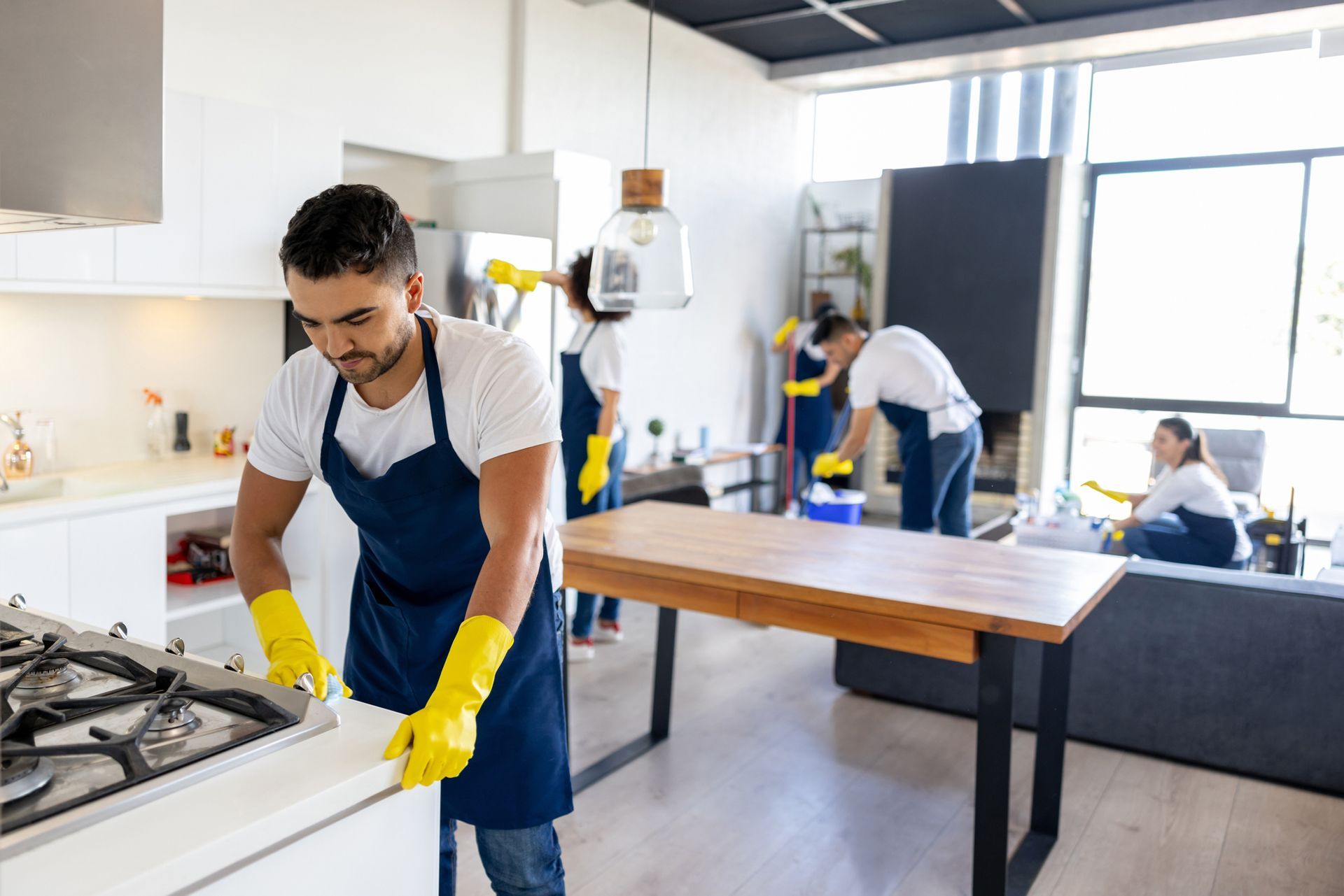 A man wearing yellow gloves is cleaning a stove in a kitchen.