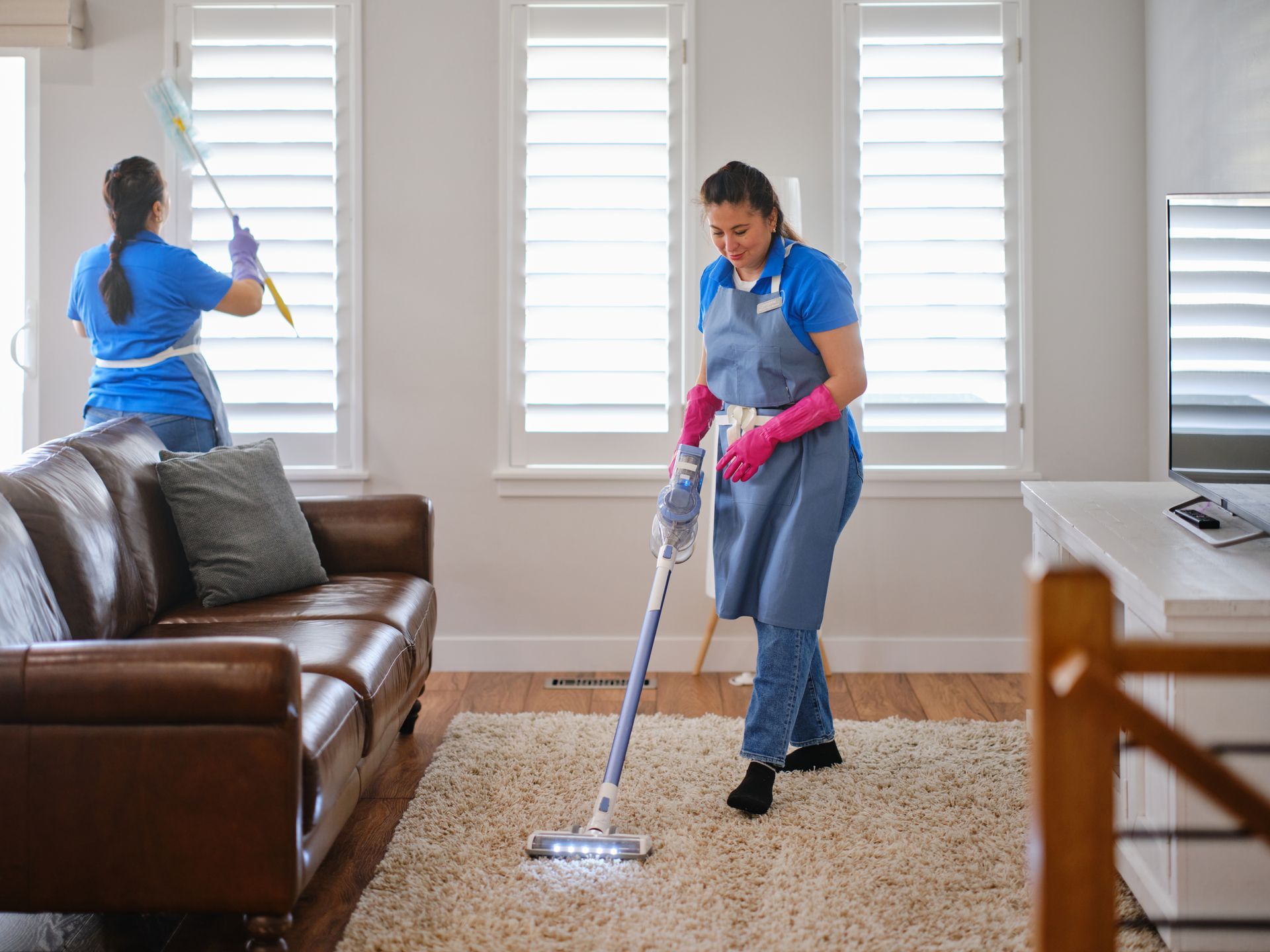 Two women are cleaning a living room with a vacuum cleaner.