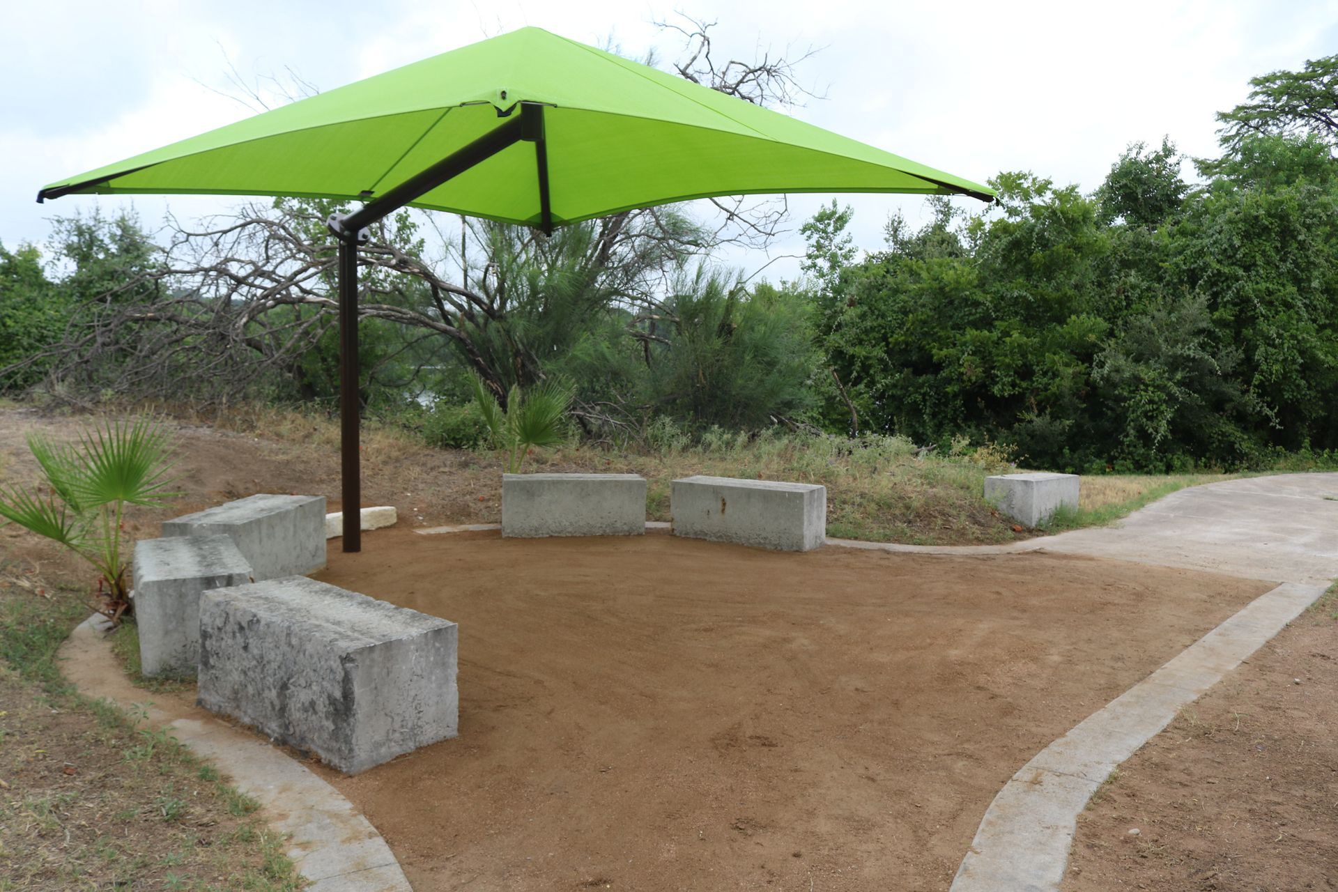 A green umbrella is sitting in the middle of a dirt area